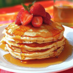 Stack of fluffy strawberry vanilla pancakes topped with fresh strawberries and a drizzle of syrup.