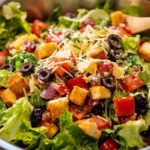 A colorful and fresh Italian salad with mixed greens, cherry tomatoes, olives, red onions, and Parmesan, topped with a zesty Italian dressing.