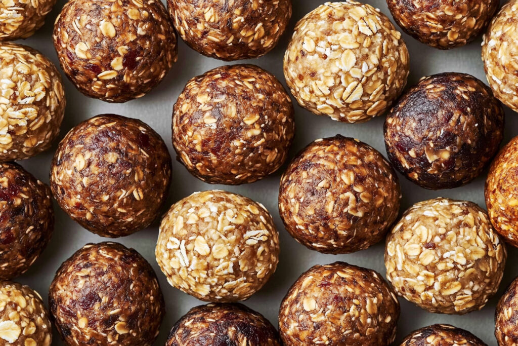 Pecan pie energy balls stacked on a white plate, with whole pecans and dates scattered around.