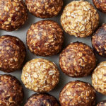 Pecan pie energy balls stacked on a white plate, with whole pecans and dates scattered around.